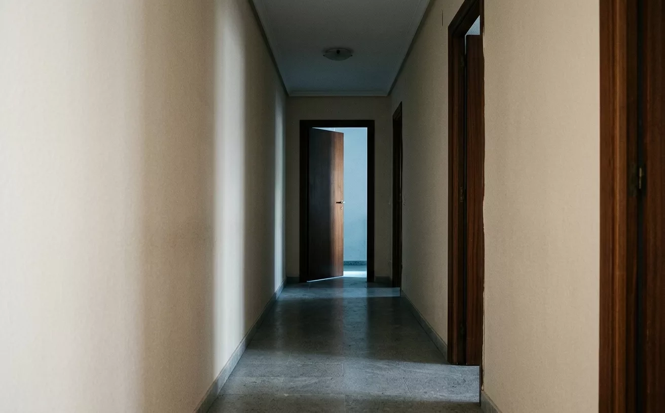 couloir vide avec porte entrouverte et lumière froide — nuit obscure de l'âme et dépression spirituelle